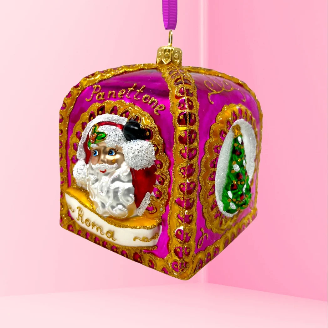 Rounded square glass Christmas ornament shown at an angle, with one face reading "Panettone" in gold script above a painted Santa face on a red background bordered in gold, resting on a white ribbon banner reading "Roma," and an adjacent face showing a green Christmas tree in a circular white inset.