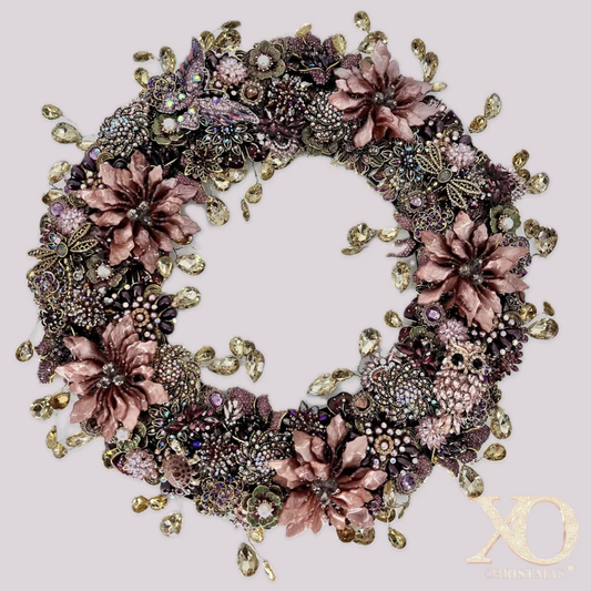 Front view, Jeweled Autumn Wreath in Dusty Mauve, a round wreath densely covered in dusty-rose enamel flowers, purple and pink rhinestones, gold filigree butterflies, faux pearls, and dangling champagne teardrop rhinestones, on a soft mauve background. XO Christmas logo in the lower right.