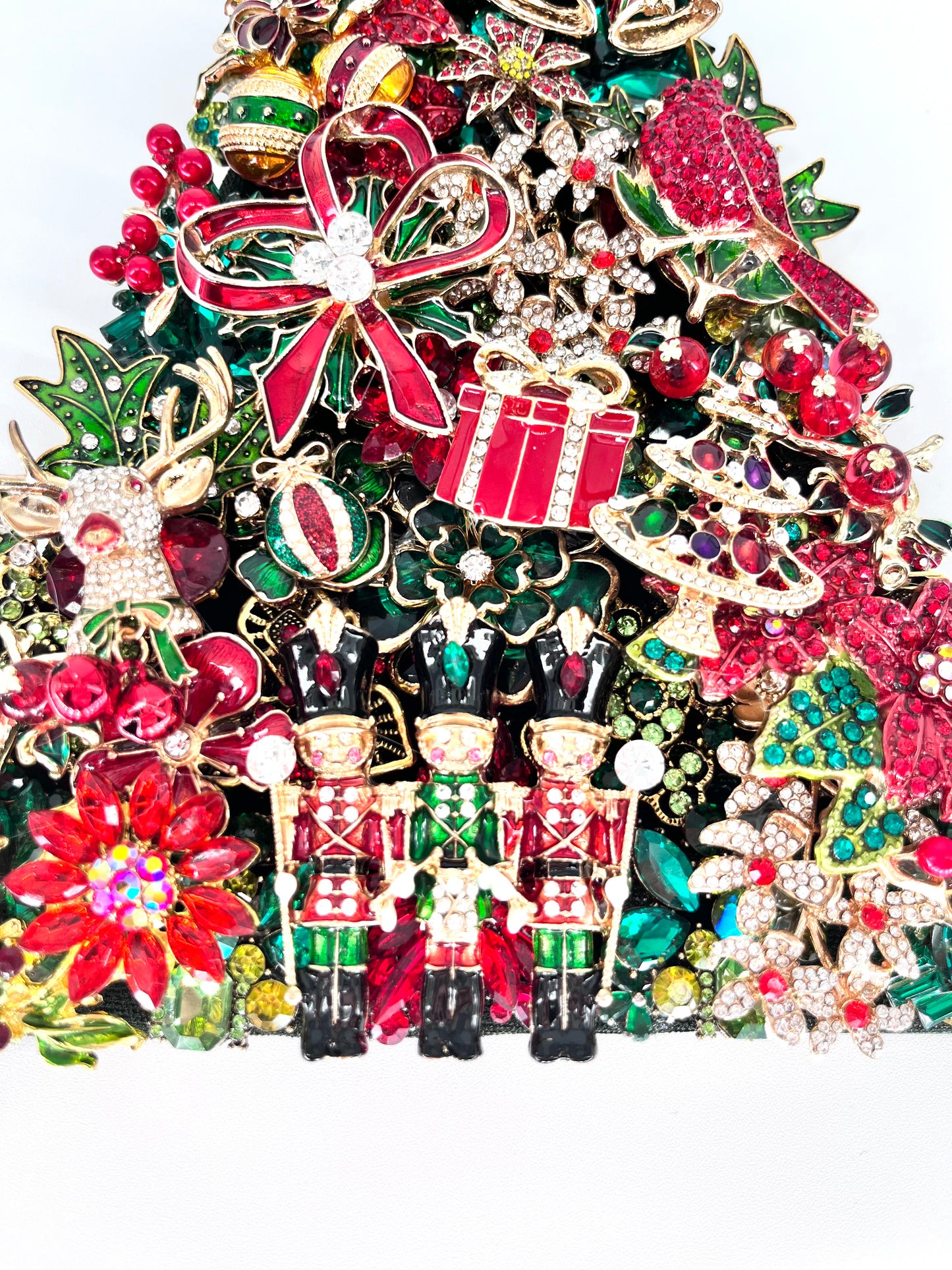 Close-up detail of jeweled Christmas tree sculpture showing rhinestone nutcracker soldiers, red bow, gift, ornaments, and poinsettia embellishments in red, green, and gold
