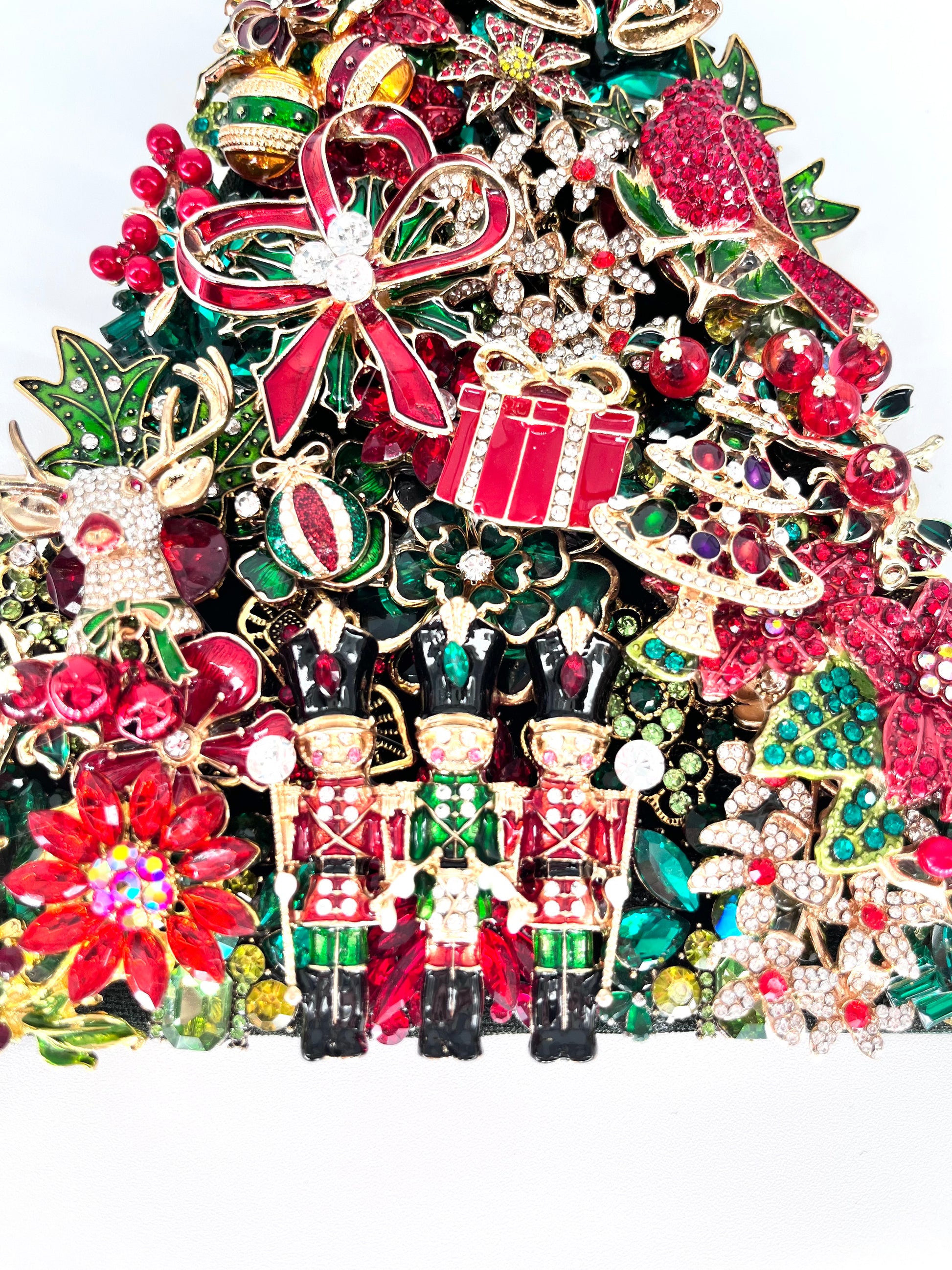 Close-up detail of jeweled Christmas tree sculpture showing rhinestone nutcracker soldiers, red bow, gift, ornaments, and poinsettia embellishments in red, green, and gold