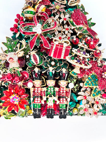 Close-up detail of jeweled Christmas tree sculpture showing rhinestone nutcracker soldiers, red bow, gift, ornaments, and poinsettia embellishments in red, green, and gold