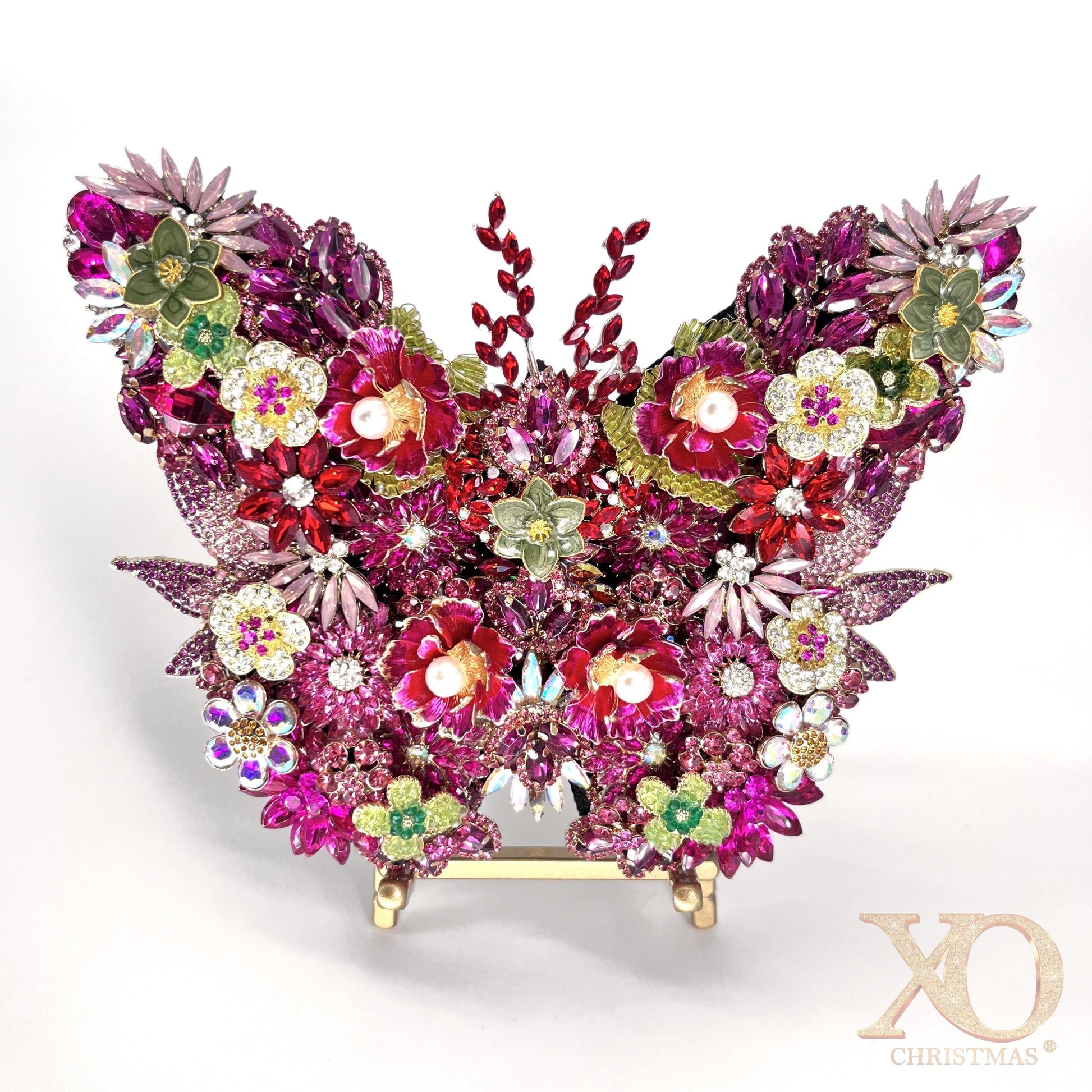 Pink Jeweled Butterfly Sculpture densely layered with fuchsia and magenta rhinestones, pearl-center floral brooches, aurora borealis accents, and sage green enamel flowers, displayed on a gold easel stand against a white background.