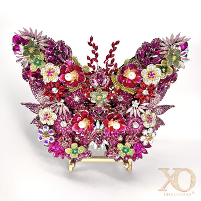 Pink Jeweled Butterfly Sculpture densely layered with fuchsia and magenta rhinestones, pearl-center floral brooches, aurora borealis accents, and sage green enamel flowers, displayed on a gold easel stand against a white background.