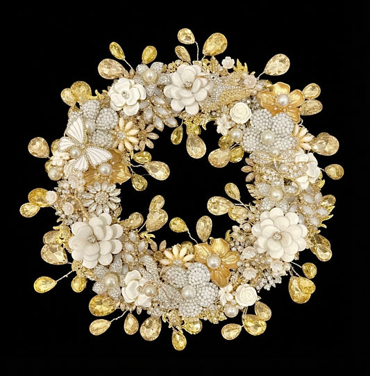A circular jeweled wreath on a solid black background, covered with white enamel flowers, faux pearl flowers, gold metallic flowers, an enamel butterfly, jeweled hummingbird, dragonfly and miniature cream roses, with faceted champagne teardrop rhinestones hanging from thin wires around both the outer edge and the inner circle.