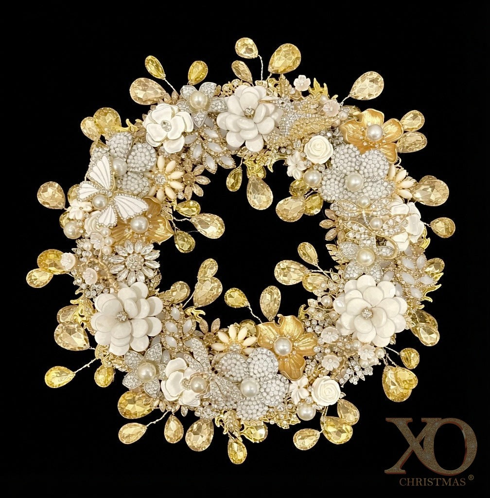 A circular jeweled wreath on a solid black background, covered with white enamel flowers, faux pearl flowers, gold metallic flowers, an enamel butterfly, jeweled hummingbird, dragonfly and miniature cream roses, with faceted champagne teardrop rhinestones hanging from thin wires around both the outer edge and the inner circle.