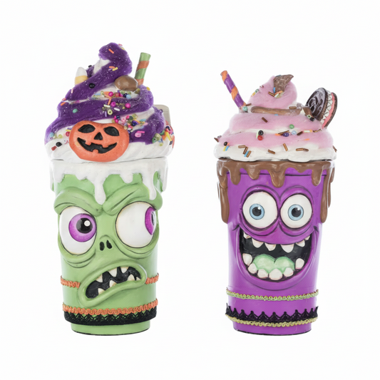 Two Halloween-themed novelty drink cups on a plain white background. The left cup is green with a zombie face and topped with a purple whipped drink, sprinkles, a jack-o'-lantern, and a light green and orange striped straw.

The right cup is purple monster milkshake cup with animated wide eyed expression with smile showing teeth and light green tongue topped with whipped cream, sprinkles, and ice cream toppers, 

