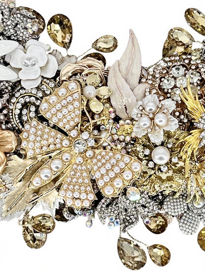A close-up detail of a jeweled wreath showcasing a golden butterfly in pearl-studded accents, white enamel florals, gold filigree leaves, champagne and aurora borealis accent
