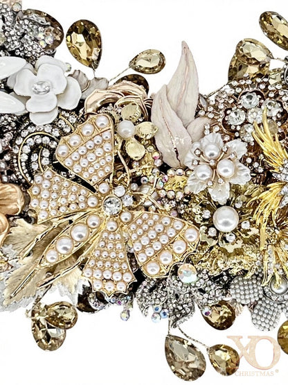 A close-up detail of a jeweled wreath showcasing a golden butterfly in faux pearl-studded accents, white enamel florals, gold filigree leaves, champagne and aurora borealis accent