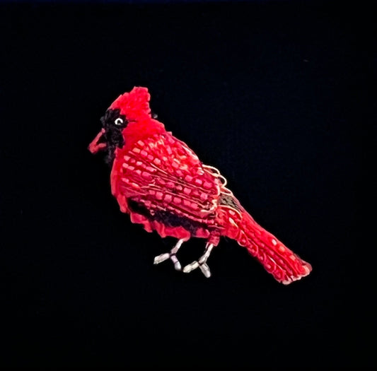 Hand-embroidered red cardinal brooch pin with a raised crest, black mask around the beak and eye, layered crimson and rose bugle-bead wings, and slim pale beaded legs.
