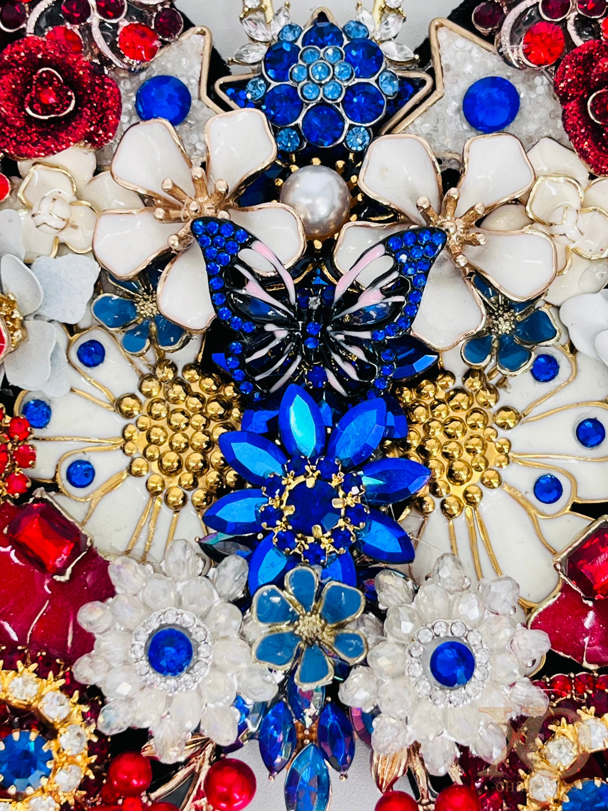 Close-up of Freedom Flight patriotic butterfly decoration. The center showing blue sapphire rhinestone butterfly, white enamel flowers, gold bead accents, and cobalt crystal details 