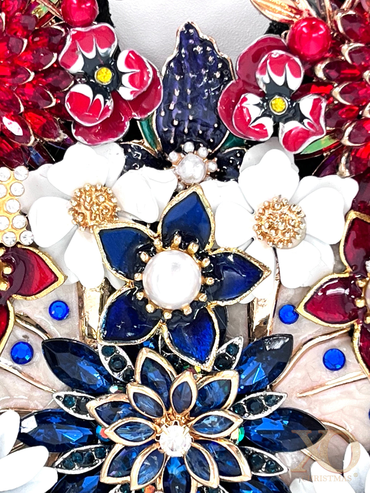 Close-up detail of patriotic jeweled butterfly decoration showing blue sapphire rhinestone flowers, white enamel blooms, red jeweled petals, and gold pearl accents 
