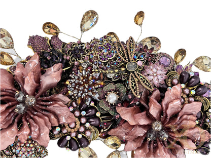 Close-up of an ornate jeweled wreath with two large dusty-rose enamel flowers, a central gold-filigree butterfly with rose-gold and rhinestone body, and clusters of purple and pink rhinestones, faux pearls, and dangling champagne teardrops.