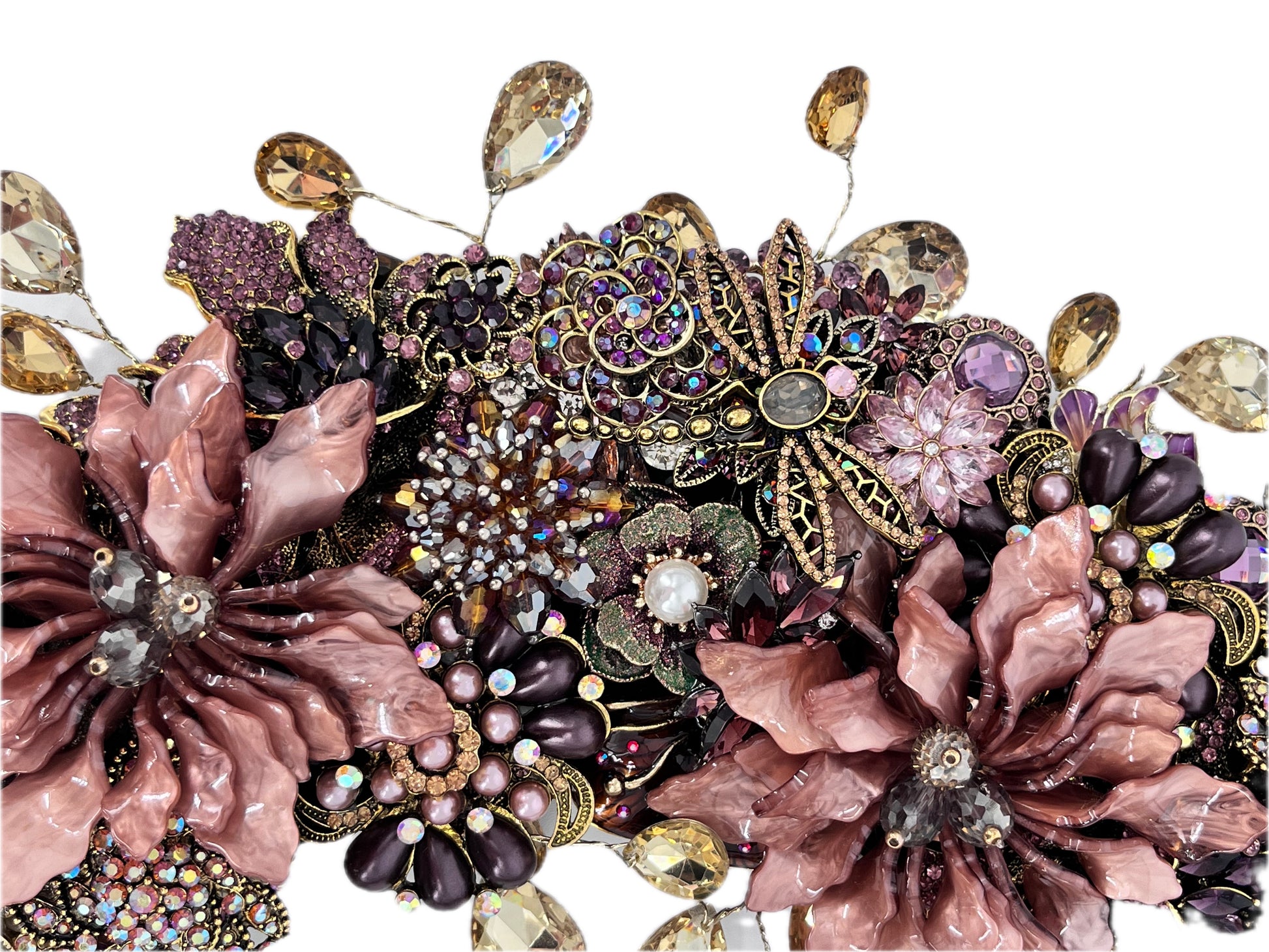 Close-up of an ornate jeweled wreath with two large dusty-rose enamel flowers, a central gold-filigree butterfly with rose-gold and rhinestone body, and clusters of purple and pink rhinestones, faux pearls, and dangling champagne teardrops.
