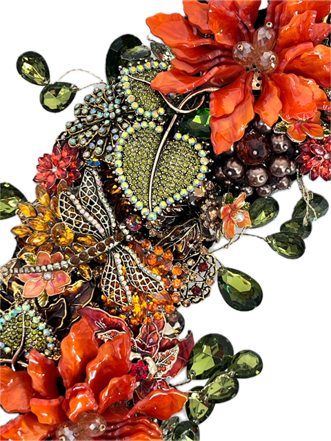 A close-up jeweled floral and leaf embellishments featuring orange and red flowers with champaign breads in center with gold accent, green teardrop rhinestones accenting the outside and inside of wreath, jeweled rhinestone dragonfly 