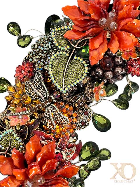 A close-up jeweled floral and leaf embellishments featuring orange and red flowers with champaign breads in center with gold accent, green teardrop rhinestones accenting the outside and inside of wreath, jeweled rhinestone dragonfly 