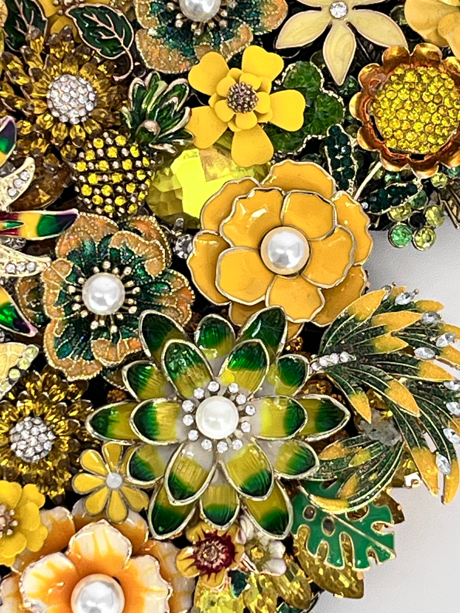 A dense arrangement of vintage-style floral brooch pins in yellow, green, and gold, featuring enamel petals, rhinestone accents, and faux pearl centers. Handmade in the USA.

