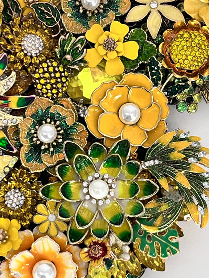 A dense arrangement of vintage-style floral brooch pins in yellow, green, and gold, featuring enamel petals, rhinestone accents, and faux pearl centers. Handmade in the USA.

