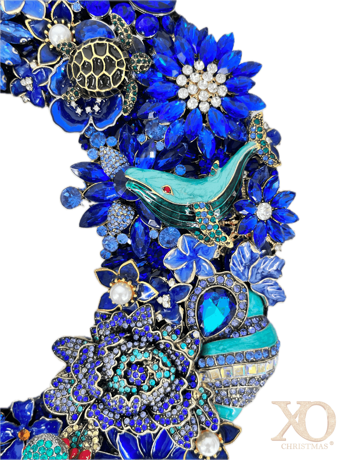 Close-up of the jeweled O on the sapphire blue rhinestone XO wall art pair, showing a sea turtle and a teal-green jeweled whale with red eye detail, framed by rhinestone starburst flowers, a rosette floral cluster, and faux pearl centers