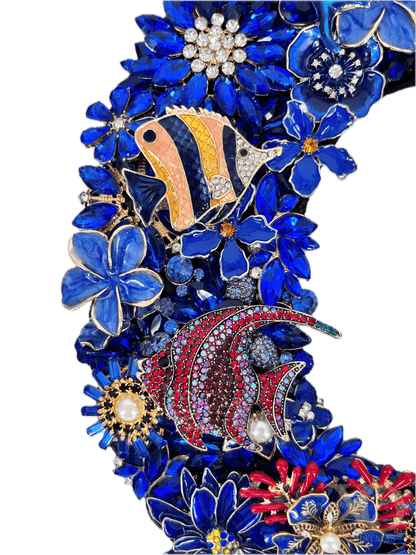 Close-up of the jeweled O on the sapphire blue rhinestone XO wall art pair, showing jewels featuring a dense floral and two jeweled fishes, heavily decorated with vivid blue enamel and rhinestones, accented with gold, red, and faux pearl accents.

