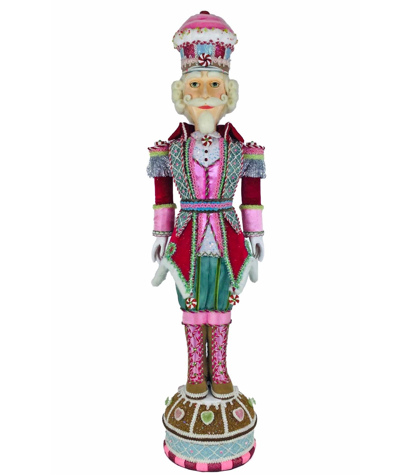 Nutcracker soldier figure with a pink frosted cupcake-shaped hat topped with a peppermint swirl, white curled hair, and a long pointed white beard, wearing a red velvet coat over a pink satin vest and light blue diamond-quilted panel, with silver tinsel epaulettes, peppermint candy appliqués, teal trousers, and pink striped boots, standing on a round gingerbread-style base decorated with icing and candy hearts.