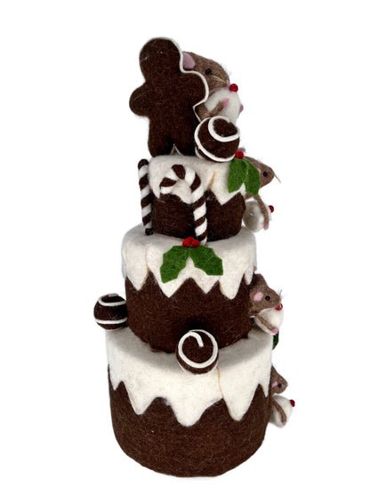Back angle of felt chocolate tiered cake centerpiece with gingerbread cookie topper, striped candy canes and holly