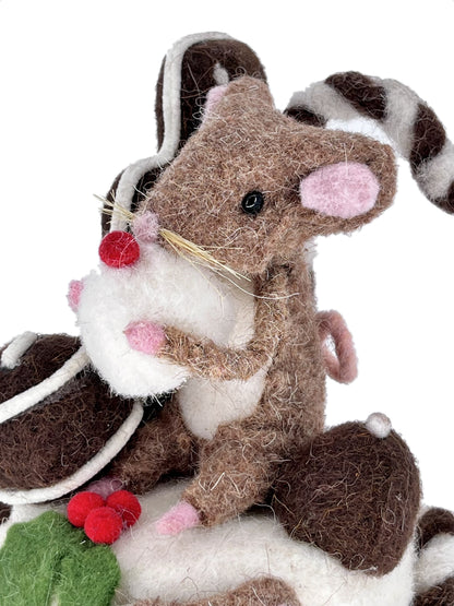 Close-up of brown felt Christmas mouse with pink ears hugging a creamy white treat on a chocolate cake
