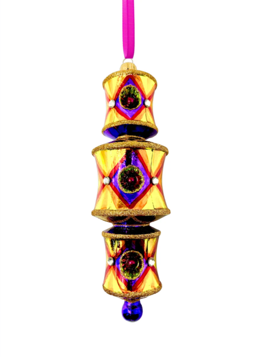 Three-tiered barrel-shaped glass ornament in gold with a red diamond lattice pattern, reflectors banded in violet and green around a maroon center, faceted crystal accents, deep blue-purple connecting sections between tiers, gold glitter trim, and a blue glass drop, hung from a magenta ribbon.