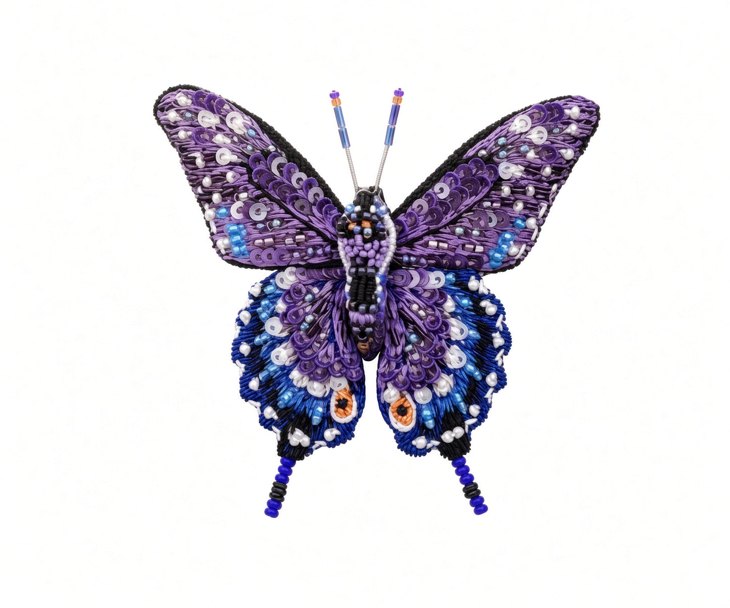 Close view of a hand-embroidered swallowtail butterfly brooch pin showing overlapping purple sequin upper wings, deep blue lower wings dotted in white beads, two orange eyespots, black wing edging, and fine beaded tails and antennae on a white background