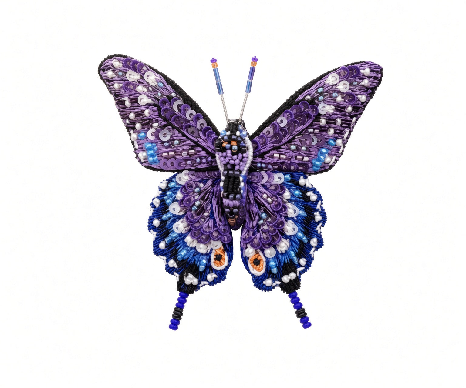 Close view of a hand-embroidered swallowtail butterfly brooch pin showing overlapping purple sequin upper wings, deep blue lower wings dotted in white beads, two orange eyespots, black wing edging, and fine beaded tails and antennae on a white background