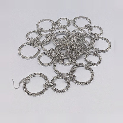 Silver garland coiled loosely on a pale gray surface, showing alternating small and large open rings, each paved in a double row of clear crystals and linked by short crystal-covered bars, with a silver wire hook at one end.