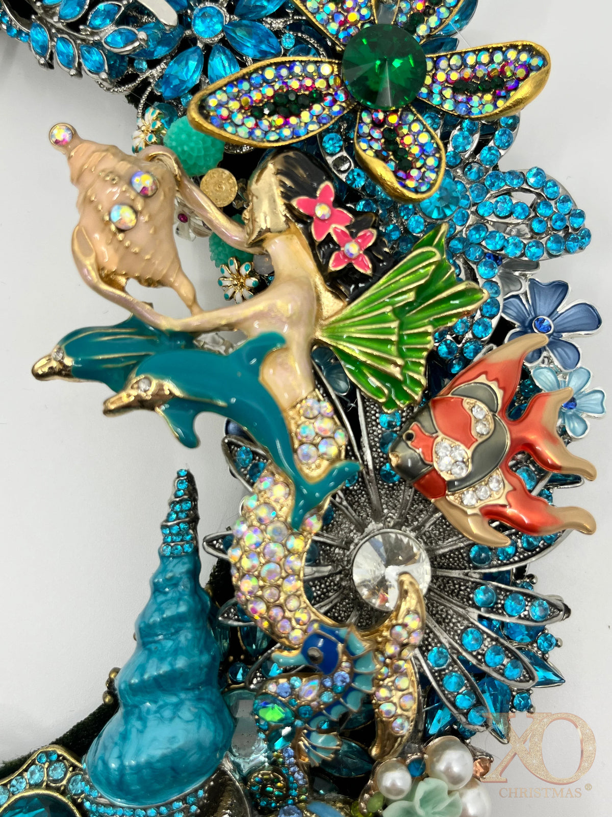 Close-up of a jeweled coastal wreath with a mermaid holding a shell, two blue dolphins, a tropical fish and rhinestone flowers.