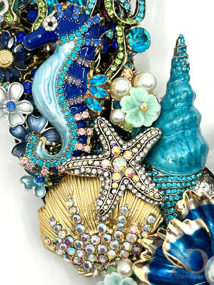 Close-up of a coastal jeweled wreath with a sapphire-blue seahorse, rhinestone starfish, gold shell and turquoise coral details.