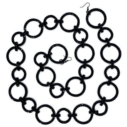 Black crystal garland of alternating large and small open circles, each set with two rows of crystals and joined by short crystal-covered bar links, coiled in a spiral on a white background with a black hook at each end.
