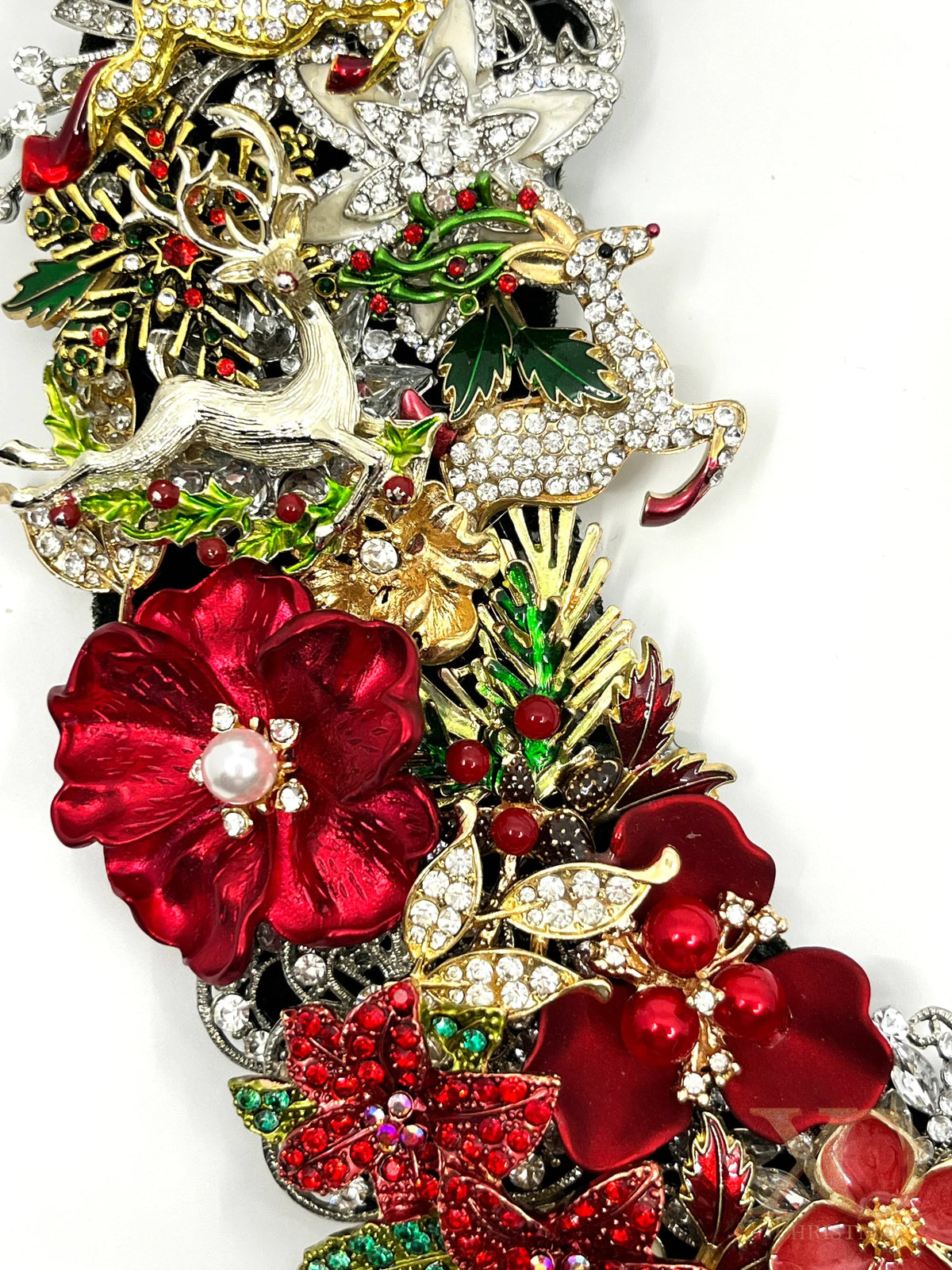 Close-up of jeweled Christmas wreath showing red enamel flowers, pearl accents, green holly, rhinestones, and silver reindeer details