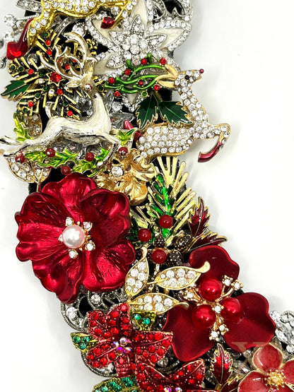 Close-up of jeweled Christmas wreath showing red enamel flowers, pearl accents, green holly, rhinestones, and silver reindeer details