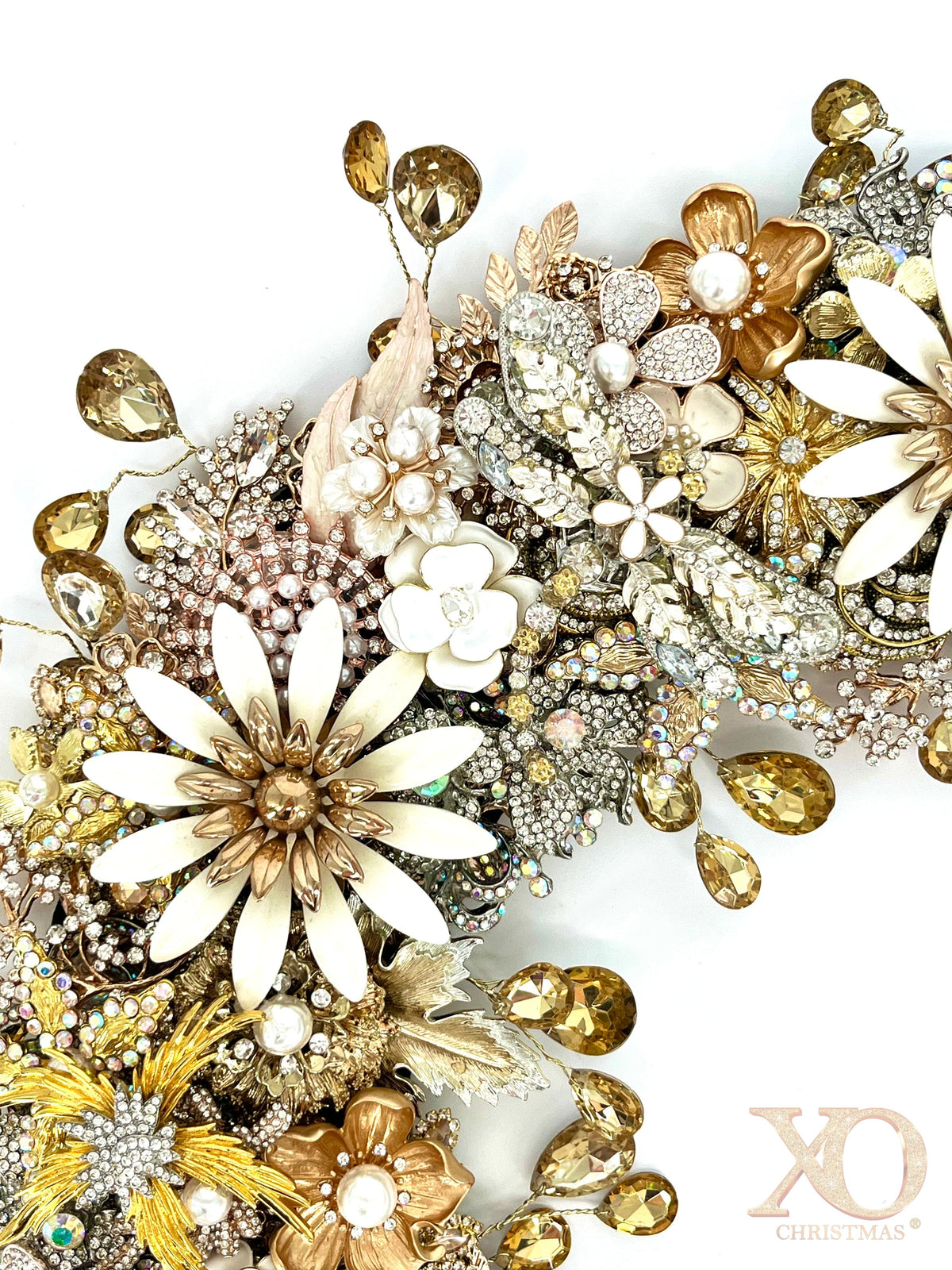 A close-up of a jeweled wreath featuring embelished jeweled dragonfly, white enamel daisy brooches, faux pearl-center florals, champagne rhinestones, gold leaf accents, and faceted amber teardrop rhinestones
