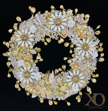  Jeweled wreath densely layered with white enamel daisy brooches, shades of gold and champagne floral clusters, faux pearl flowers, and faceted champagne teardrop rhinestones against a black background.