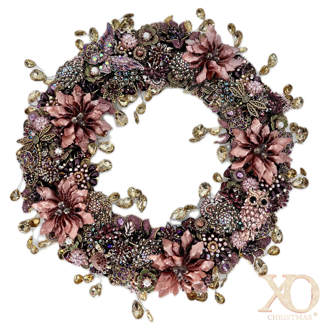 Full view of an ornate circular jeweled wreath densely covered in dusty-rose enamel flowers, purple and pink rhinestone clusters, faux pearls, gold colored filigree, butterflies, and other floral motifs, with champagne-colored teardrop rhinestones dangling from both the outer and inner edges.