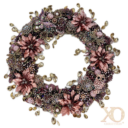 Full view of an ornate circular jeweled wreath densely covered in dusty-rose enamel flowers, purple and pink rhinestone clusters, faux pearls, gold colored filigree, butterflies, and other floral motifs, with champagne-colored teardrop rhinestones dangling from both the outer and inner edges.