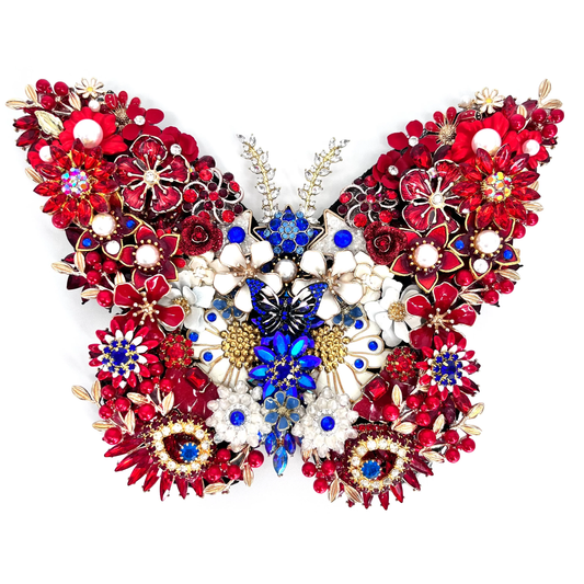 A highly detailed, symmetrical butterfly-shaped jeweled  decorative piece composed of red, white, and blue floral elements with gold-toned metal settings, shown against a plain white background. 