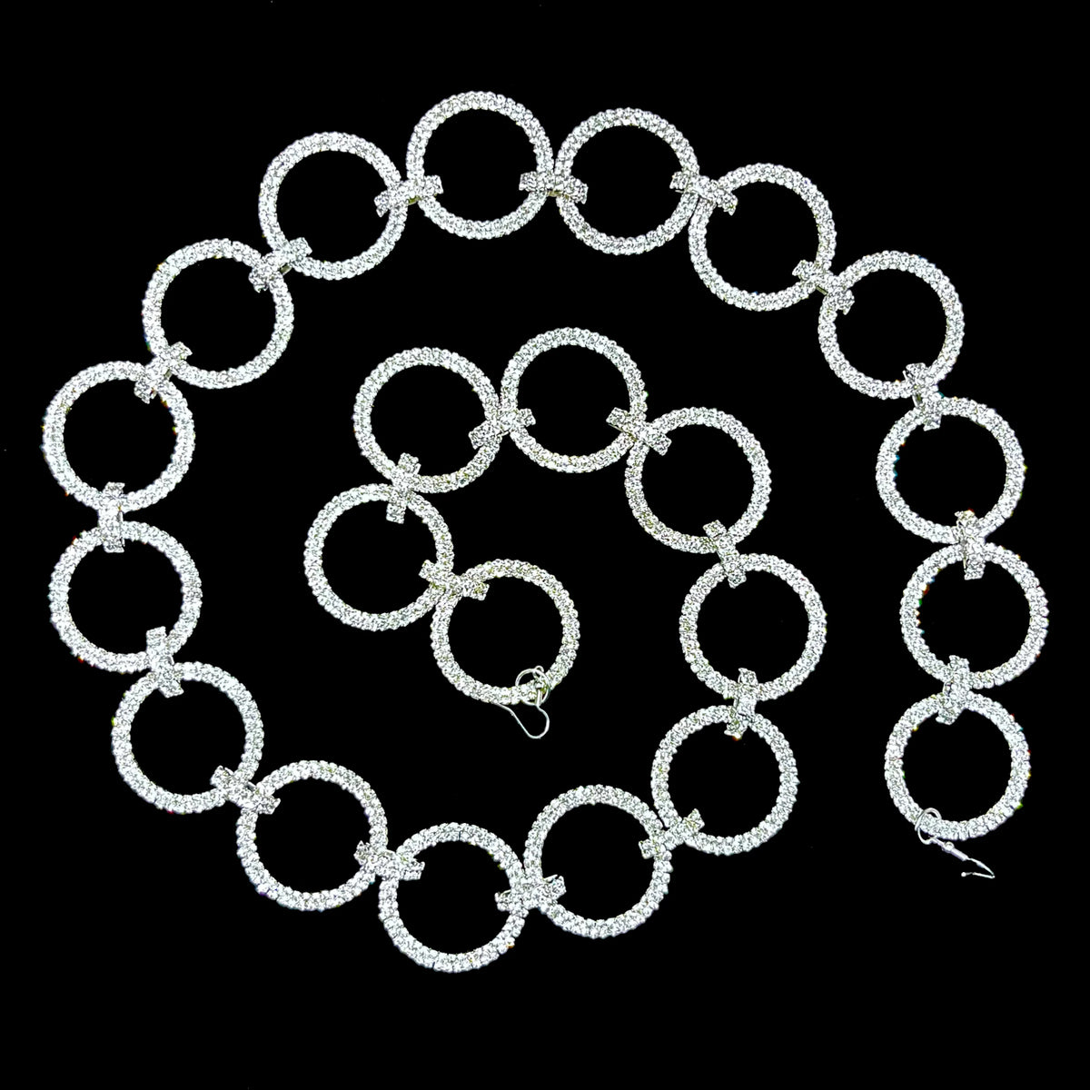 Silver garland of large, uniform open rings densely set with clear crystals, joined by small crystal-studded clasps and coiled in a spiral on a black background, with a wire hook at each end.