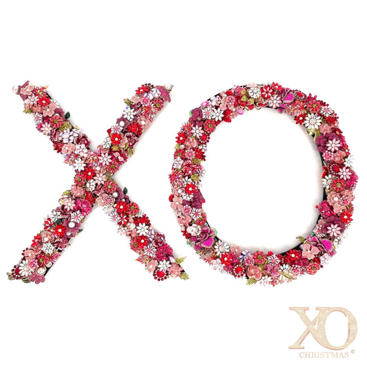 Large jeweled letter X and O letter covered in layers of rhinestone florals in various shades of pink, red, and fuchsia and faux pearl embellishments with sage green leaf accents 