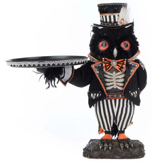 Front view of an ornately dressed black-feathered Halloween owl butler figure with orange eyes, white beak, an orange satin bow tie with cameo brooch, a rhinestone ribcage motif on the chest, black-and-white striped trousers, and clawed feet on a log base