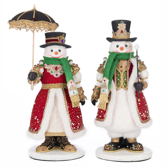 Katherine's Collection Sir Frosty Banks and Dame Icy Banks, a jeweled snowman pair in red velvet coats with white fur trim, jeweled crown-topped hats, and gold beaded embellishments — Sir Frosty holding a cane and monocle, Dame Icy with a lace-trimmed parasol.