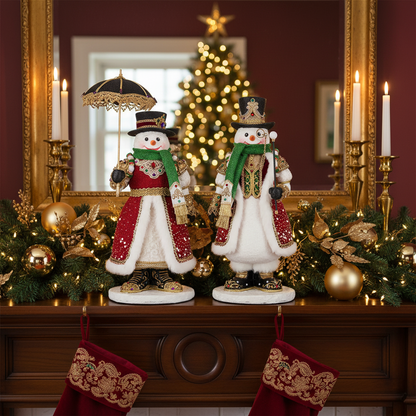 Katherine's Collection Sir Frosty Banks and Dame Icy Banks displayed on a mantel in front of a gold-framed mirror, flanked by candlesticks, garland, and a lit Christmas tree, showing the jeweled snowman pair's red velvet coats and crowned top hats in a styled holiday setting.