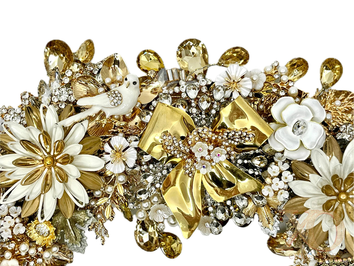 Close-up of vintage polished gold bow and ivory jeweled wreath showing a jeweled white dove, white enamel flowers, faux pearls, and champagne crystal drops
