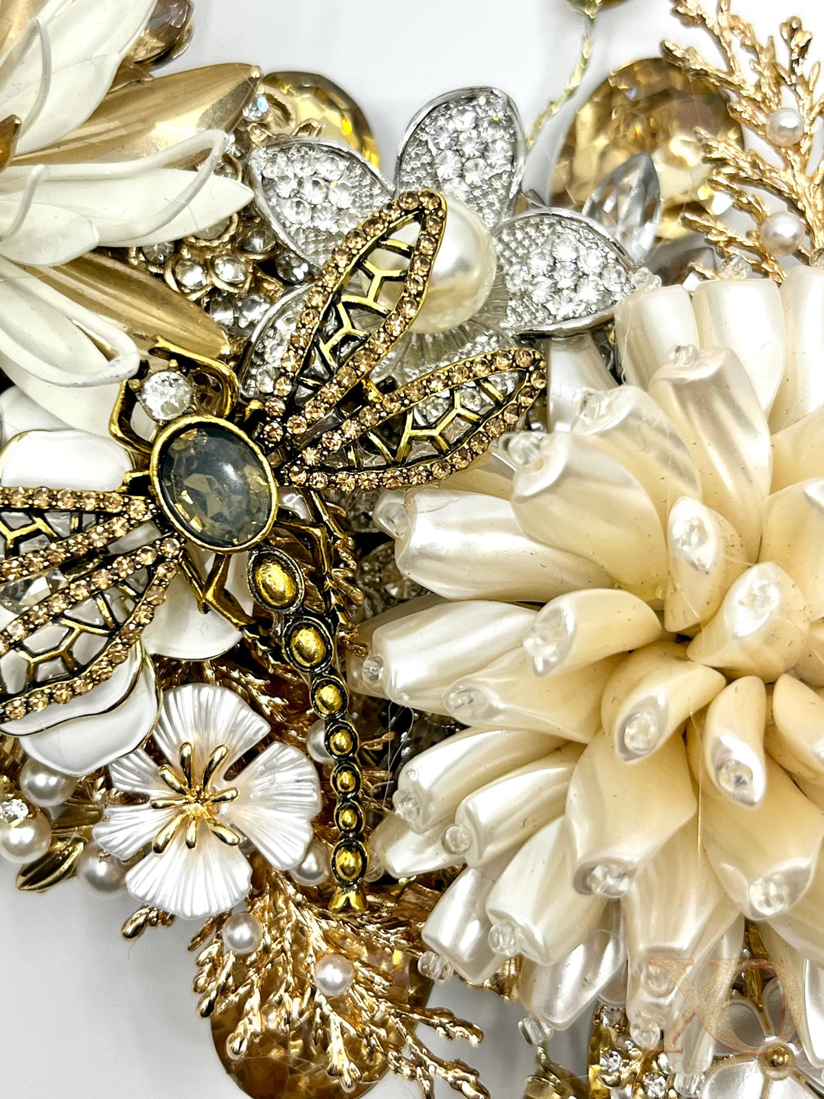 Macro detail of gold and ivory jeweled wreath featuring a jeweled dragonfly brooch with smoky center stone, rhinestone-encrusted wings, cream dahlia flower, white enamel blooms, and faux pearls