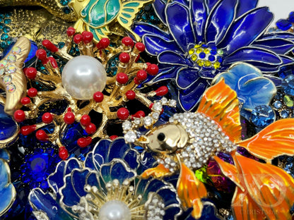 Close-up of Deep Blue coastal jeweled wreath showing gold fish, red coral, pearls, and blue enamel flower brooches.
