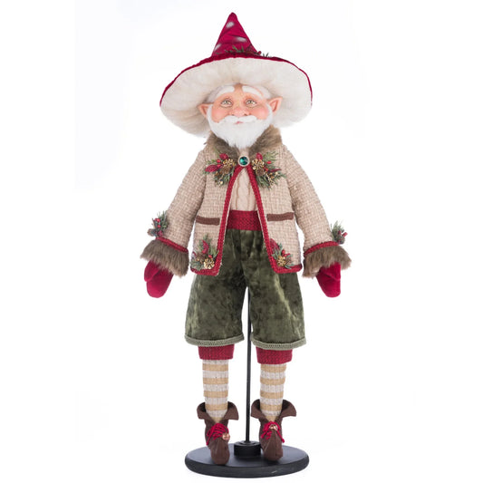 Front view of William Woodear Elf figure on its round black stand, showing pointed ears, snowy beard, burgundy polka-dot hat with pine sprig trim, tan tweed jacket with jeweled clasp, sage green velvet trousers, striped stockings, and curled brown elf shoes with bells