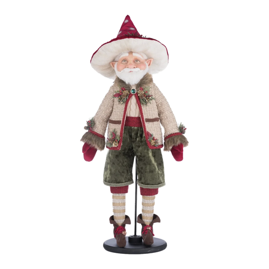Front view, William Woodear Elf figure on its round black stand, with pointed ears, a white beard, and a warm smile, wearing a wide-brimmed polka-dot burgundy hat trimmed in cream fur and pine sprigs, a tan tweed jacket with faux fur lining and a jeweled clasp, sage green velvet trousers, striped stockings, and curled brown elf shoes with bells